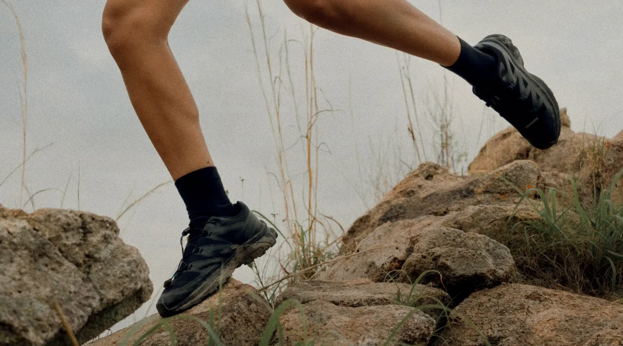 A trail runner in black merino socks and trail shoes leaping across rocks