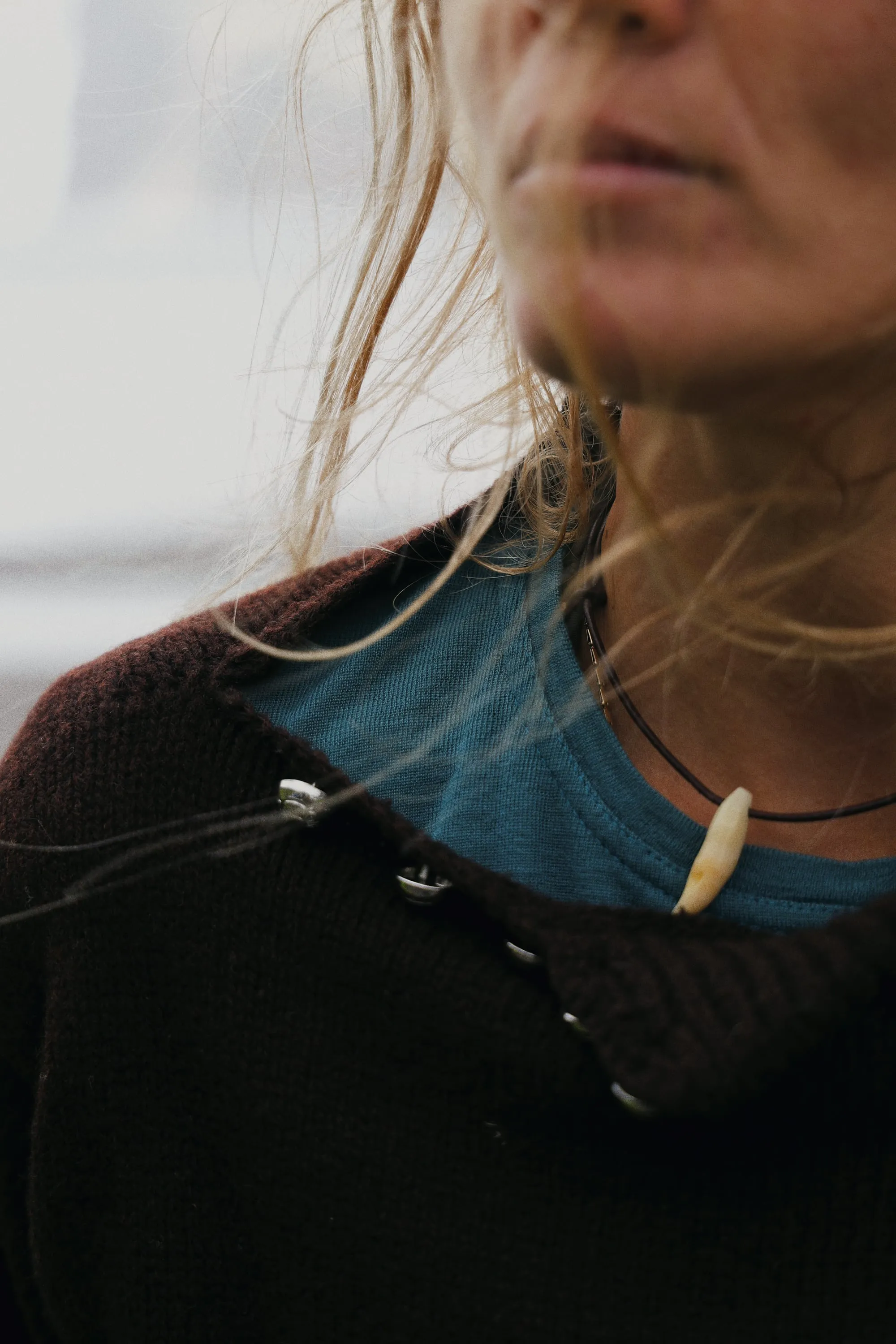 Close-up of a woman in a brown knit cardigan over a teal merino T-shirt, hair blowing across her face