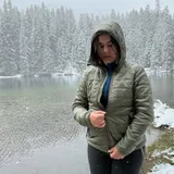 Женщина в куртке цвета Olive с поднятым капюшоном у заснеженного озера